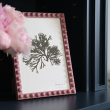 Load image into Gallery viewer, An A4 handcrafted pink bobbin frame on a sitting room shelf with a vase of peonies beside it