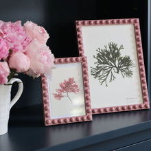 Load image into Gallery viewer, The A4 pink bobbin frame alongside te 5x7" bobbin frame in pink on a shelf in a sitting room next to a vase full of pink peonies