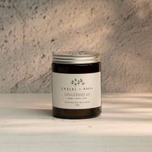 Load image into Gallery viewer, The Gingerbread scented soy wax candle from Embers &amp; Roots shown in a dark amber glass jar candle with a silver metal lid and a white paper label reading 'Embers + Roots Gingerbread', set on a light wooden surface against a textured gray wall.