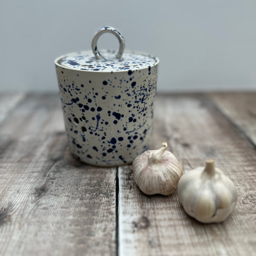 A handmade garlic pot on a wooden table with some fresh garlic bulbs next to it 