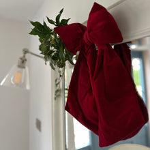 Load image into Gallery viewer, Red velvet bow hanging on a white mirror with ivy and foliage.