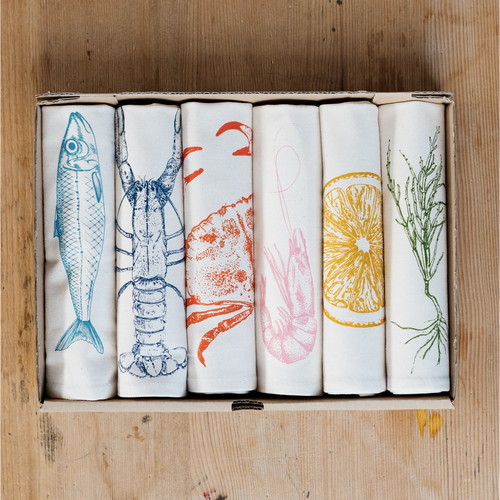 Set of six folded towels with hand drawn seafood illustrations on a wooden table