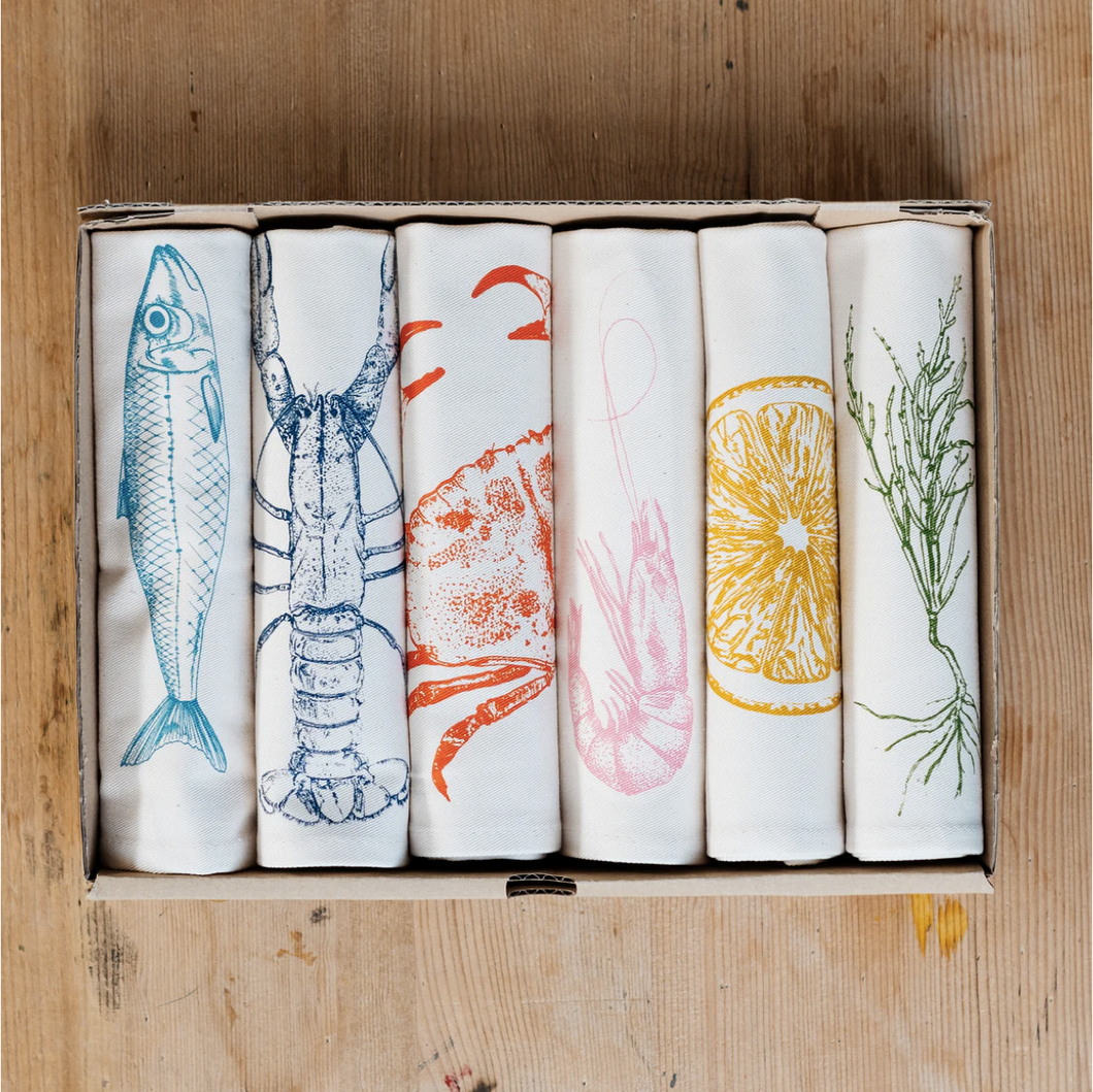 Set of six folded towels with hand drawn seafood illustrations on a wooden table