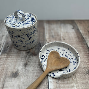 A handmade set of a splatterware garlic pot and spoon rest on a wooden table