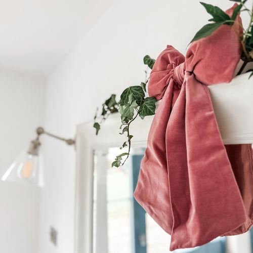 A handmade dusty pink velvet bow hanging over a mirror with ivy and miseltoe