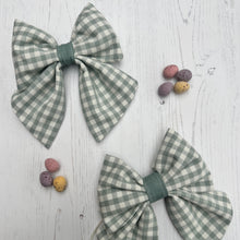 Load image into Gallery viewer, a pair of handmade bows in duck egg blue gingham with some mini eggs on a table
