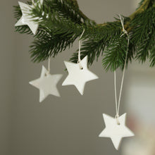 Load image into Gallery viewer, Handmade porcelain stars hanging from the branch of a christmas tree