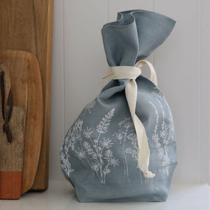 Handmade breathable linen bread bag in duck egg blue on a white kitchen counter against some chopping boards