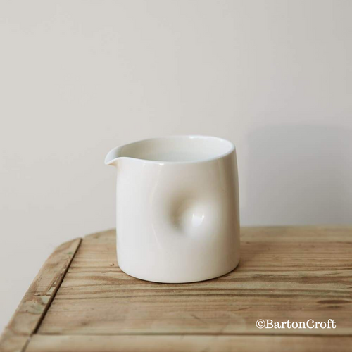 Handmade Dimpled Jug by Barton Croft in a Milk Glaze, sat atop a wooden stool