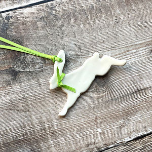 A close up image of the handmade ceramic running hare with a fresh satin green ribbon 