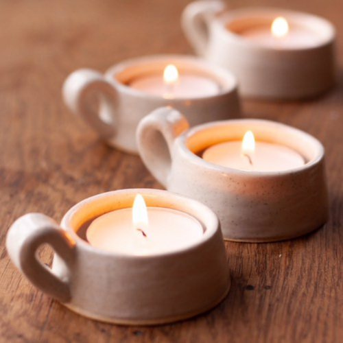 A group of handmade rustic handled tealight holders with tealights lit on a table