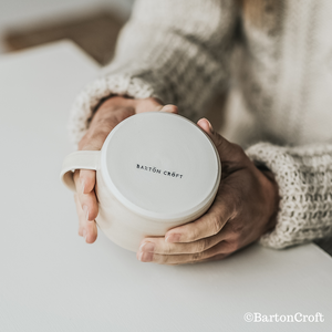 A woman holding a Barton Croft mug showing the logo on its underside