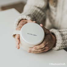 Load image into Gallery viewer, A woman holding a handmade Barton Croft mug showing the bottom of the mug which is unglazed with the Barton Croft logo