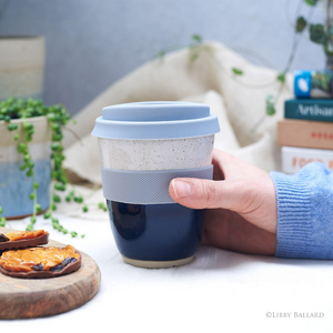 A hand holding the Handmade travel mug with band by Libby Ballard in her midnight glaze