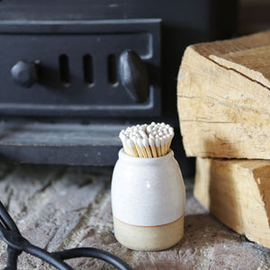 Handmade white match striker by a fireside next to some logs and fire tongs